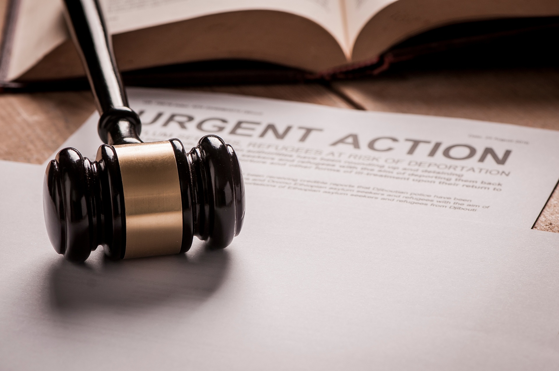 A gavel rests on a blank piece of paper next to a book and a document that reads urgent action at the top.